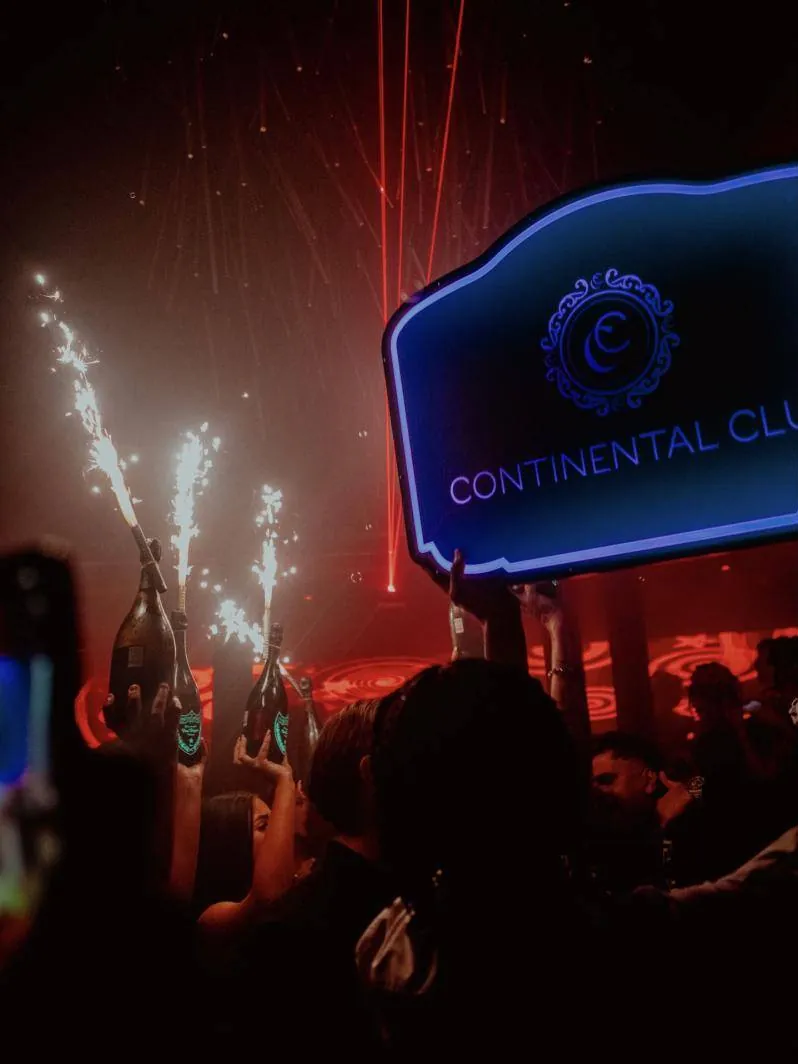 Bottles with sparklers held up under the illuminated Continental Club sign