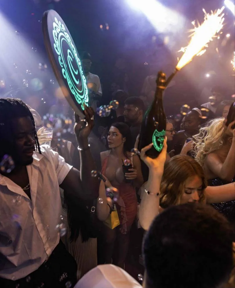 A host carrying the lit Continental crest through the crowd beside a sparkler bottle